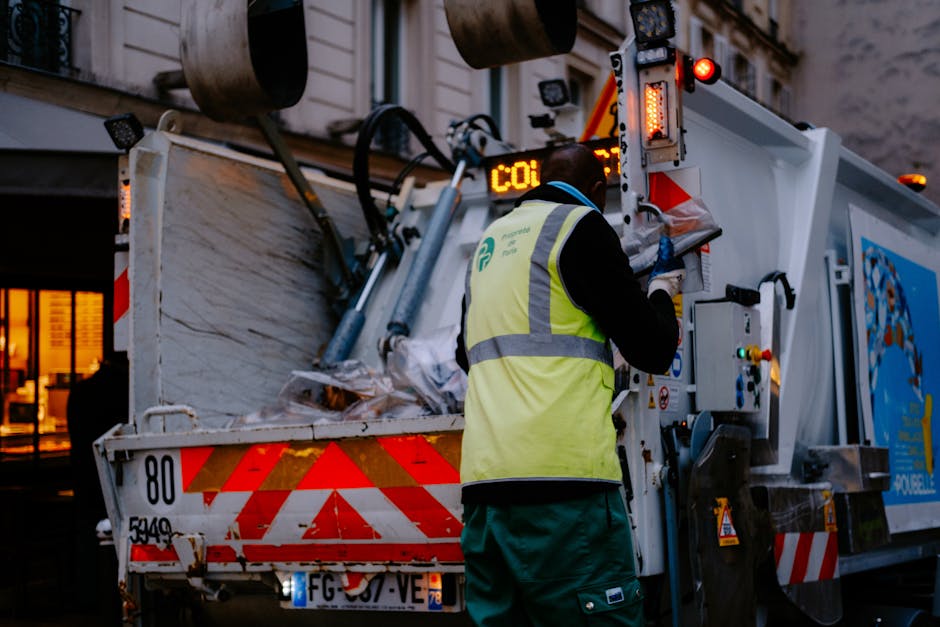 The image shows the rear side of a white commercial van parked on a street outside a building with glass doors and windows. Three blue heavy-duty plastic rubbish bags, filled and tied at the top, are